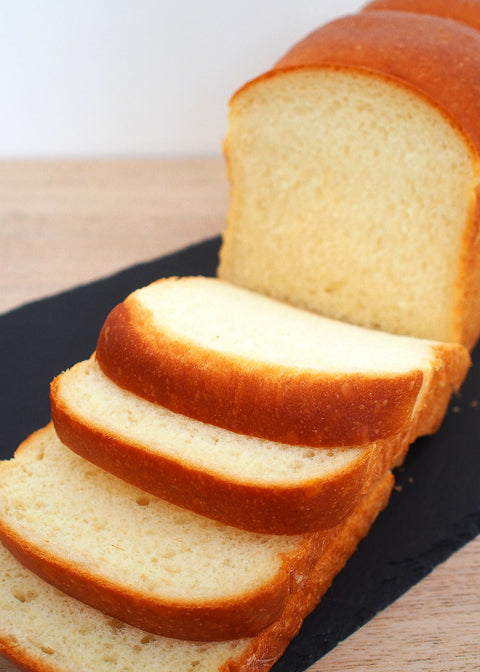 Sliced loaf of bread on a black plate with a white background