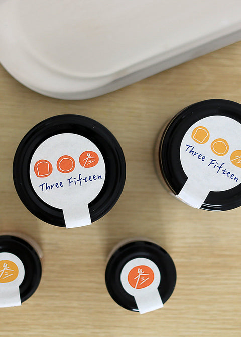 Four containers with 'Three Fifteen' labels on a wooden surface