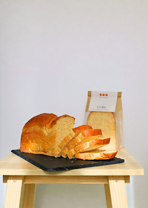 Loaf of bread with slices on a black slate board on a wooden stand against a plain background