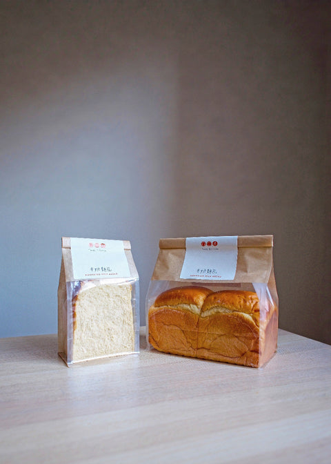 Two packages of bread on a wooden surface with a plain background